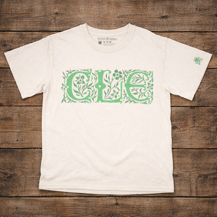 White t-shirt with green floral 'CLE' design on a wooden surface