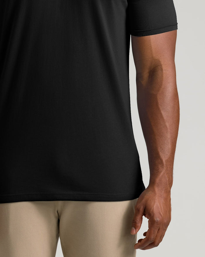 Close-up of a person wearing a black short-sleeve athletic T-shirt and light beige pants against a plain light gray background.