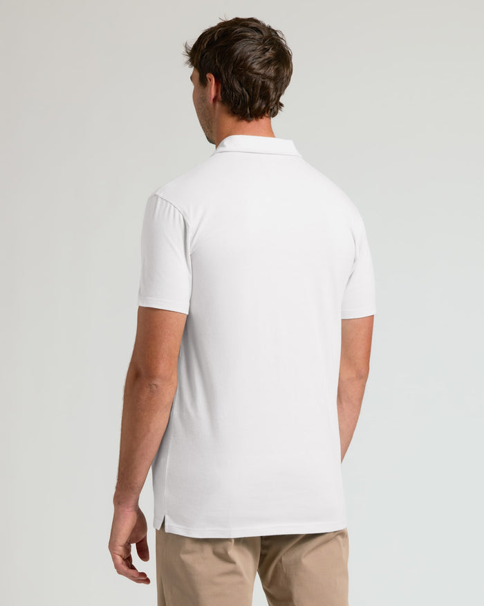 A man viewed from the back wearing a white short-sleeve polo shirt and khaki pants against a light gray studio background.