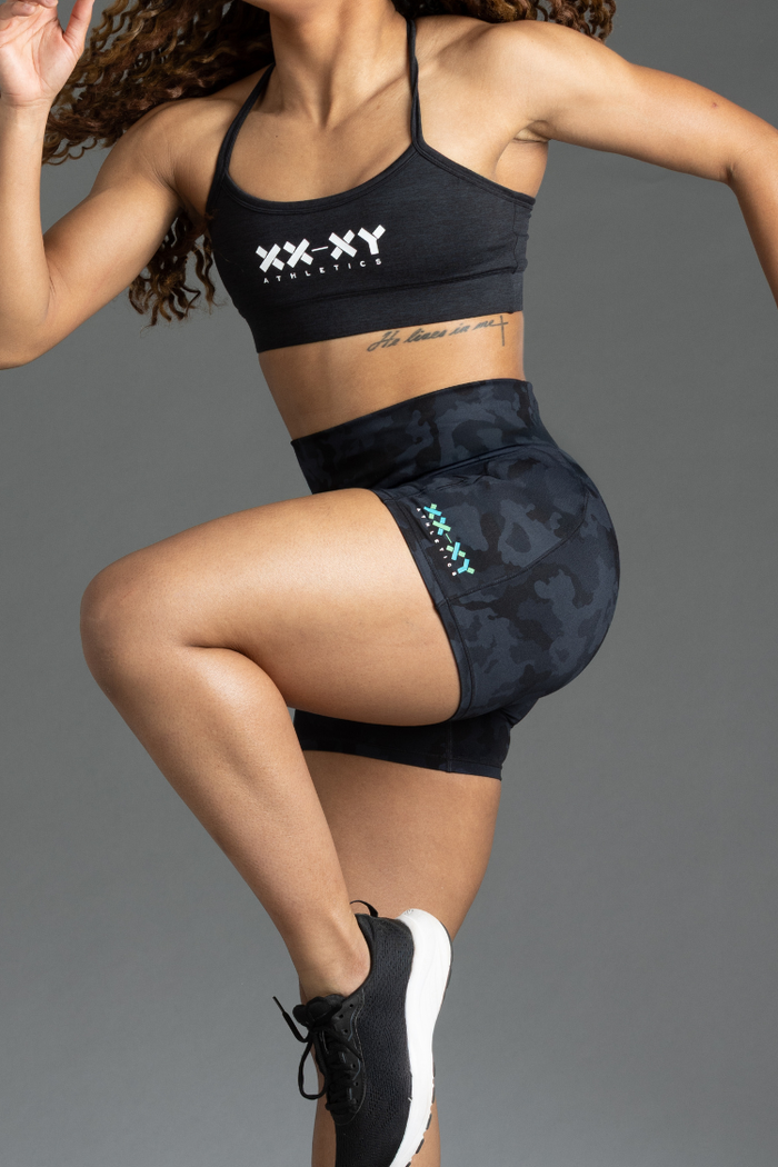 Person wearing black sports bra and shorts with visible branding on a gray background || Black Camo