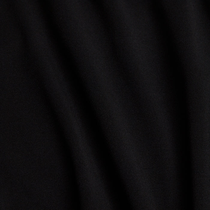 Close-up of the Black - Q-Zip’s soft, matte fabric shows gentle folds and subtle shadows. The smooth surface features moisture-wicking properties, with light accentuating raised areas and deepening the rippled black creases.
