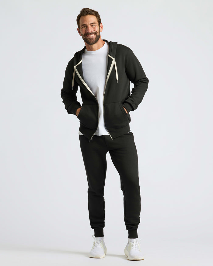 Man wearing Black Fleece French Terry Zip Hoodie with hands in pockets.