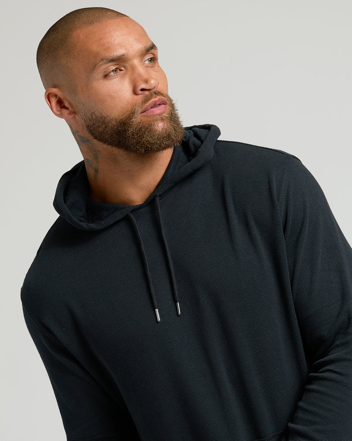 Man wearing Black Waffle Hoodie with kangaroo pocket, against gray background.