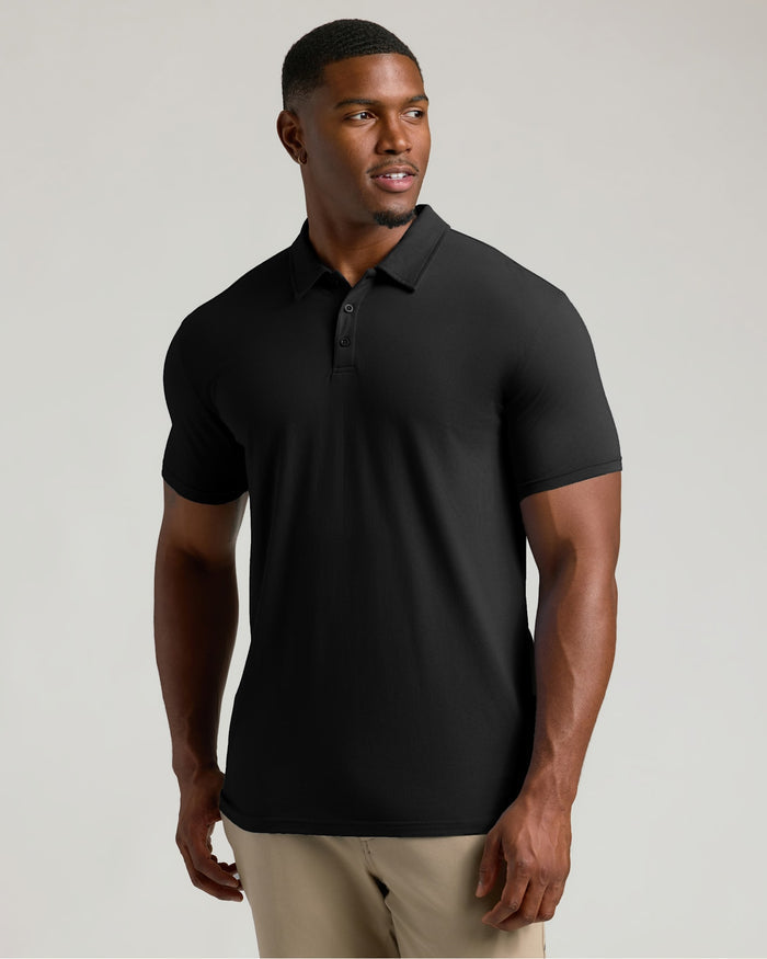 A man wearing a black short-sleeve polo shirt and khaki pants, standing against a light gray studio background.