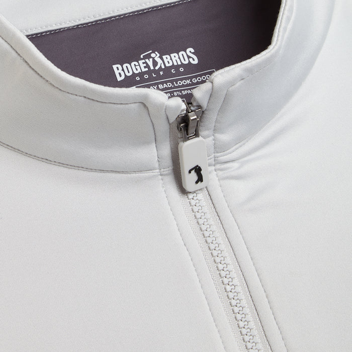 Close-up of the Bone Q-Zip white jacket with an athletic fit, highlighting the collar and unique golfer-shaped zipper pull. Inner label shows Bogey Bros Golf Co. and the tagline "Play Bad, Look Good.
