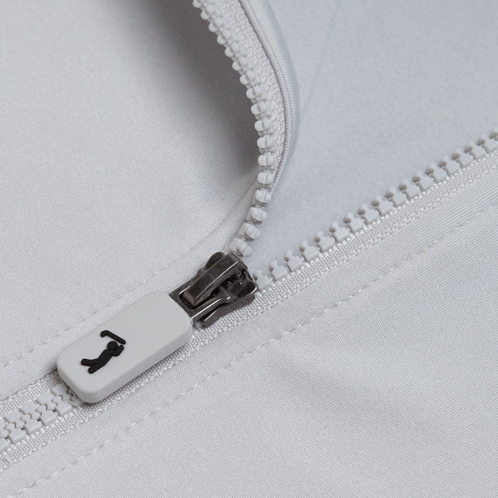 Close-up of the Bone - Q-Zip's white plastic zipper, partially unzipped on light gray, moisture-wicking fabric. The zipper pull displays a small black icon resembling a stylized seated figure.