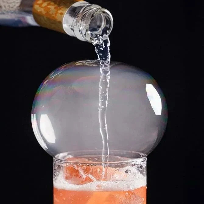 Bottle pouring liquid into a glass with a colorful, smoke bubble sphere.