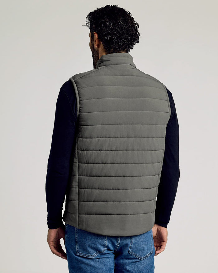 Man wearing a gray Carbon Puffer Vest over a black long-sleeve shirt and blue jeans, shown from the back against a neutral background.