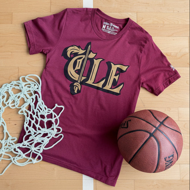 Maroon t-shirt with 'CLE' design, basketball, and net on a wooden surface