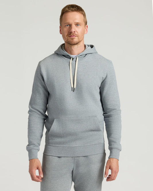 A man wearing a Dark Heather Gray Fleece French Terry Pullover Hoodie with a front kangaroo pocket and adjustable cream-colored drawstrings, styled as men's basics.
