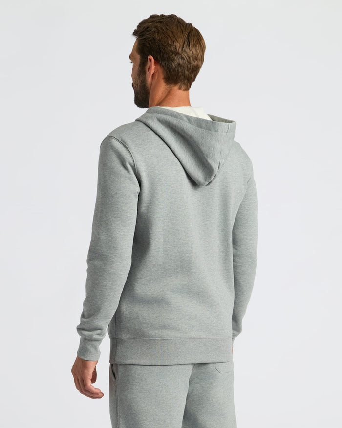 A man wearing a light gray heathered hoodie and matching sweatpants, shown from a rear three-quarter view against a plain light gray studio background.