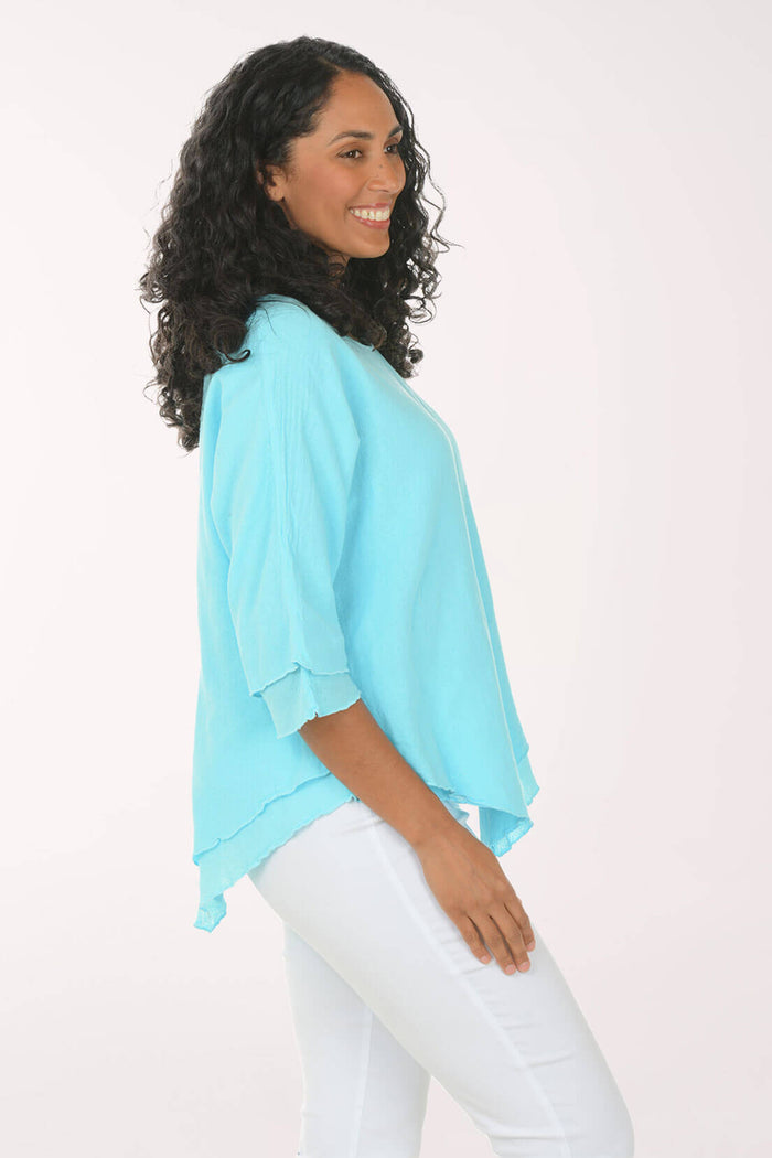Side shot of a woman wearing a light blue top and white pants on a white background