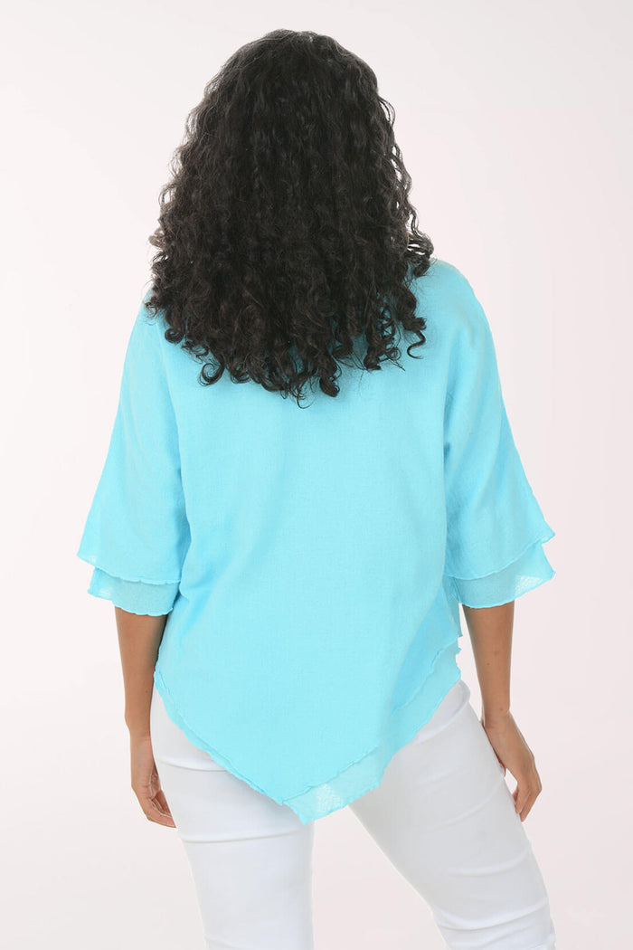 Back shot of a woman wearing a light blue top and white pants on a white background