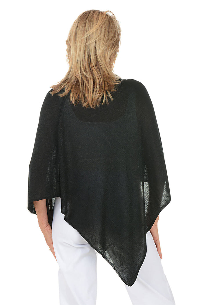 Woman wearing a black poncho over a white outfit on a white background. Back shot
