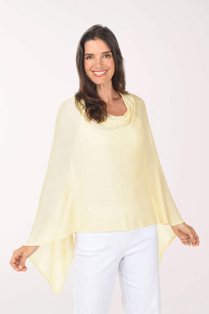 Woman wearing a light yellow poncho over a white top and pants on a white background