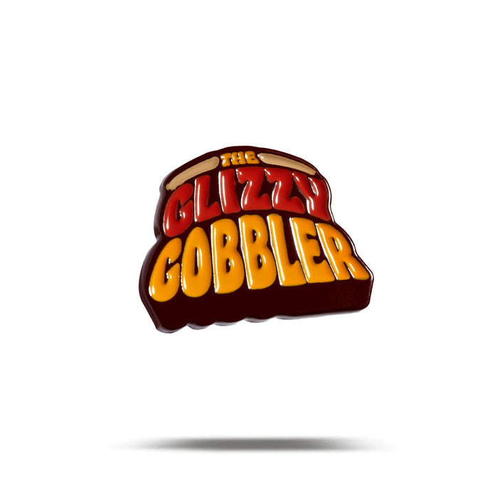 A glossy enamel ball marker shaped like a hot dog bun, displaying "The GLIZZY GOBBLER" in bold yellow and red. Finished with iron nickel plating, the Glizzy Gobbler Ball Marker is shown centered on a white background with a faint shadow below.
