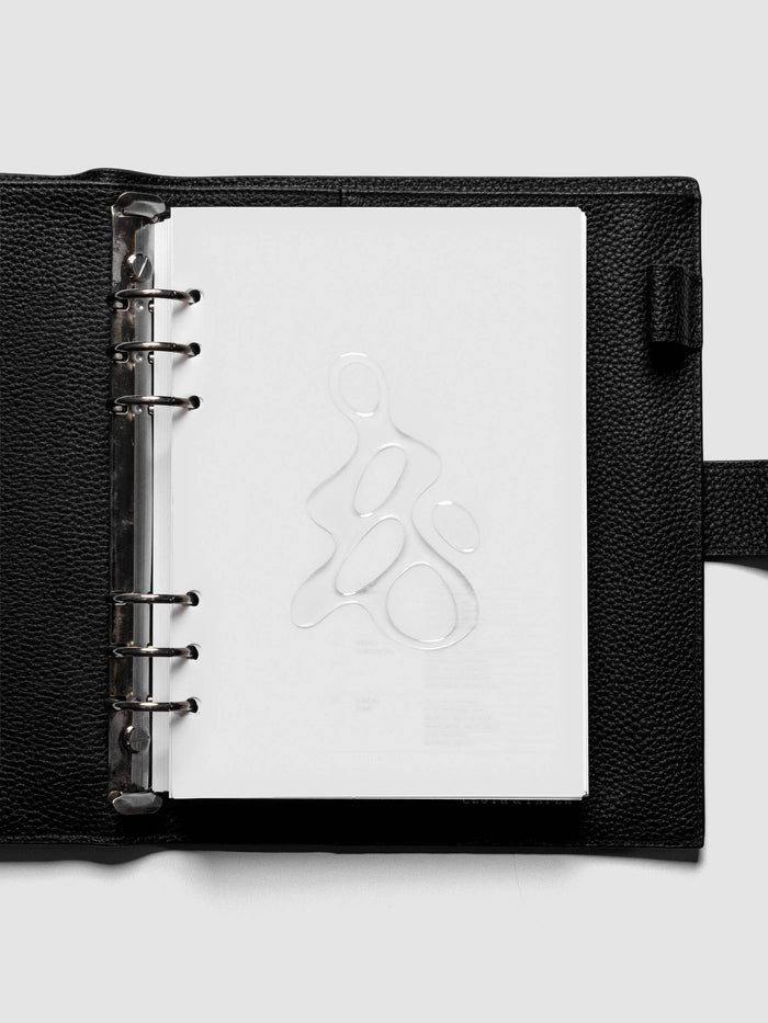 Light grey, semi-transparent, and glossy plastic planner dashboard with organic raised shape design in size A5 shown ringbound in a black leather agenda.