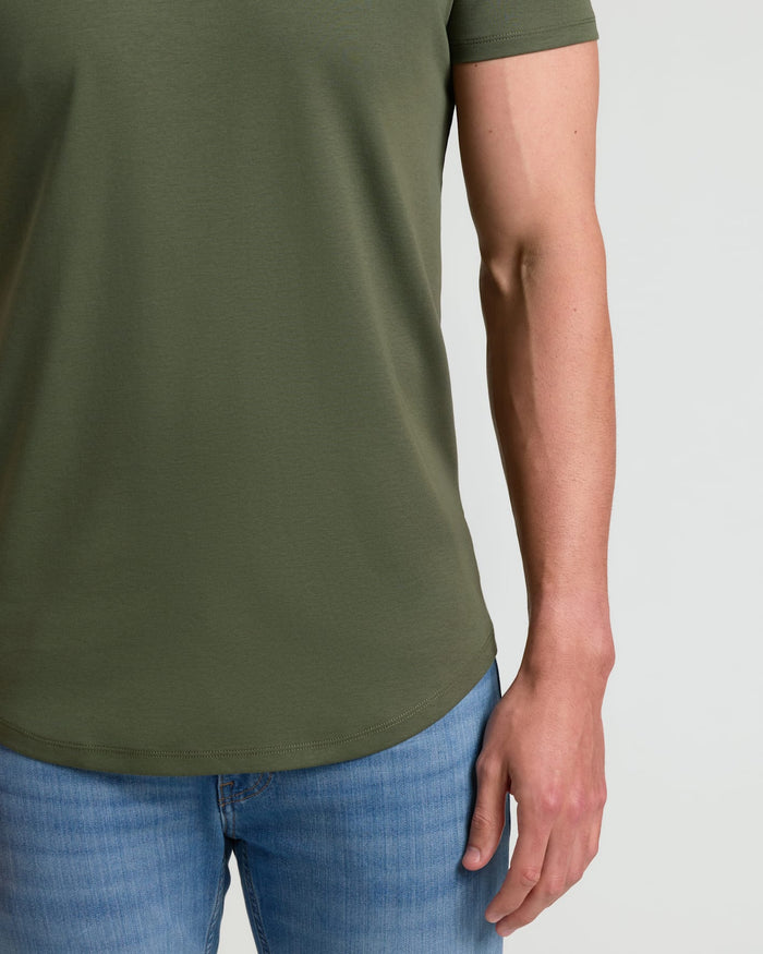 Close-up of a man wearing an olive green Grove Tall Pima Cotton Blend Curved Hem Crew shirt paired with light blue jeans, showcasing the curved hem detail on a casual men's basics look.