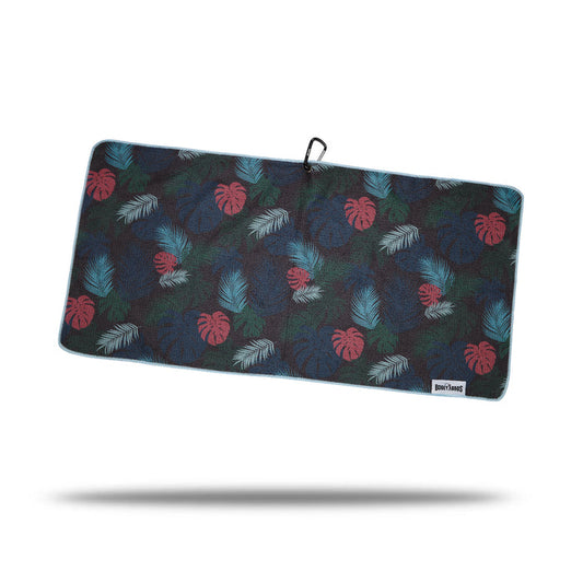 The Haolie Nights - Towel is a rectangular microfiber towel with a dark background, double-sided print of red and blue monstera leaves plus teal palm fronds. It features blue edging, a clip and eyelet loop at the top, and a white tag in the bottom right corner.