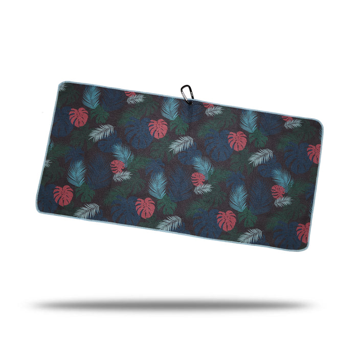 The Haolie Nights - Towel is a rectangular microfiber towel with a dark background, tropical leaf print in green, blue, and red, light blue trim, black clip and eyelet at the top, dual-sided print design, and a subtle shadow beneath.