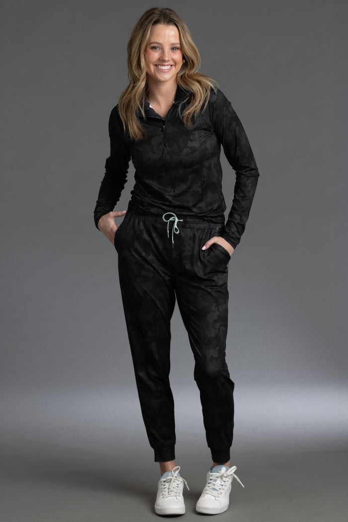Woman wearing a black outfit with white sneakers on a gray background || Black Camo