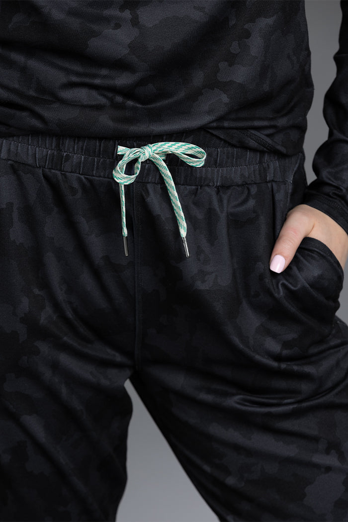 Black camouflage pants with a green drawstring on a gray background || Black Camo