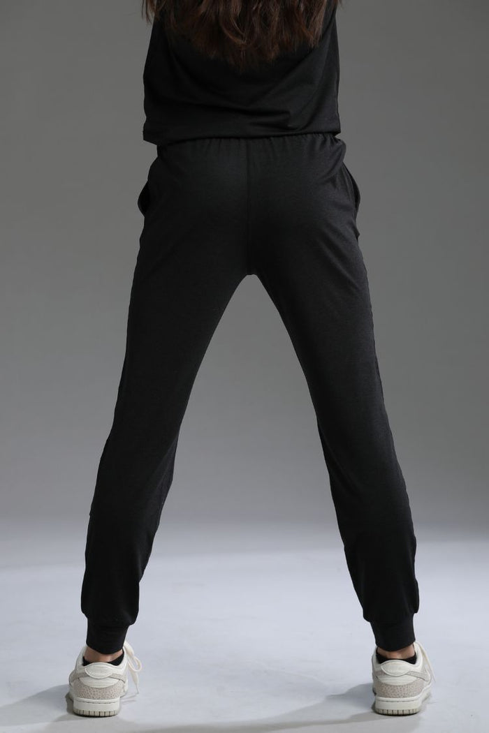 Person wearing black jogger pants and a dark hoodie on a gray background || black
