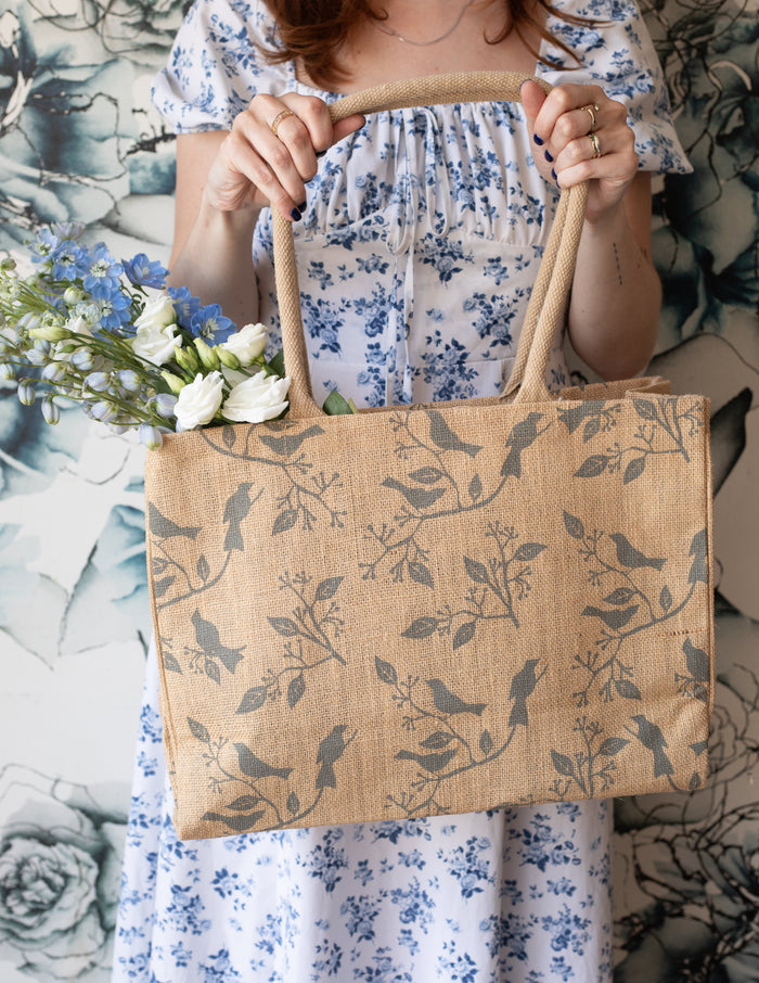 A person holding a beige jute tote bag with a bird print.