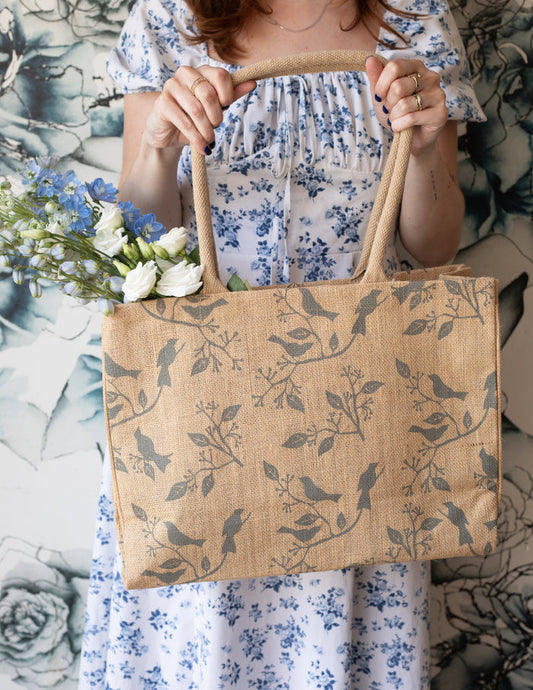 A person holding a beige jute tote bag with a bird print.