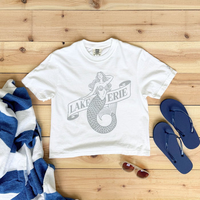 White t-shirt with mermaid graphic and 'Lake Erie' text on a wooden surface with beach accessories.