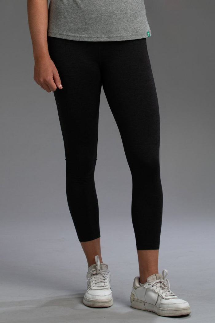 Person wearing black leggings and white sneakers on a gray background || Black Heather