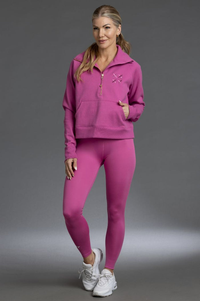 Woman wearing a pink tracksuit with a logo on a gray background || Bright Fuchsia