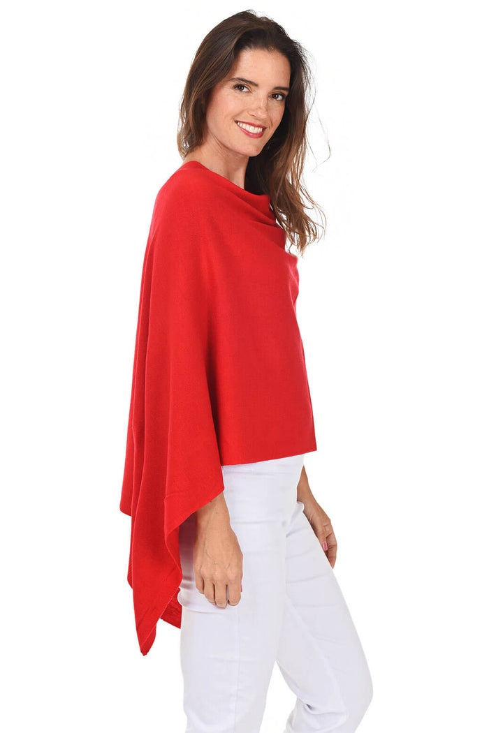 A woman wearing a red popover poncho with white pants. Side shot.