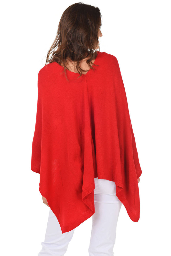 A woman wearing a red popover poncho with white pants. Back shot.