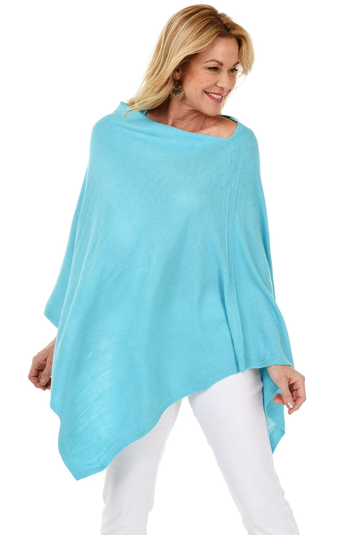 A woman wearing a blue popover poncho with white pants.