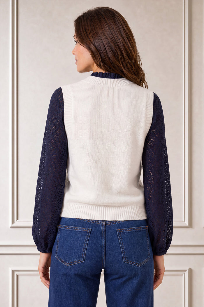 Model wearing the Aspiga Merino Wool Knitted Short Tank in Ivory over a navy lace blouse with jeans, back view