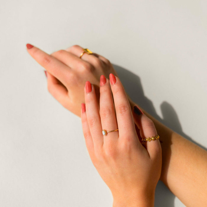 BKIND Cancer coral nail polish on hands with gold rings, photographed in natural light
