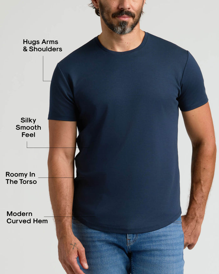Man wearing a navy blue Pima Cotton Blend Curved Hem Crew 4-Pack t-shirt with a modern curved hem, silky smooth fabric, and a fit that hugs arms and shoulders while being roomy in the torso, paired with blue jeans.