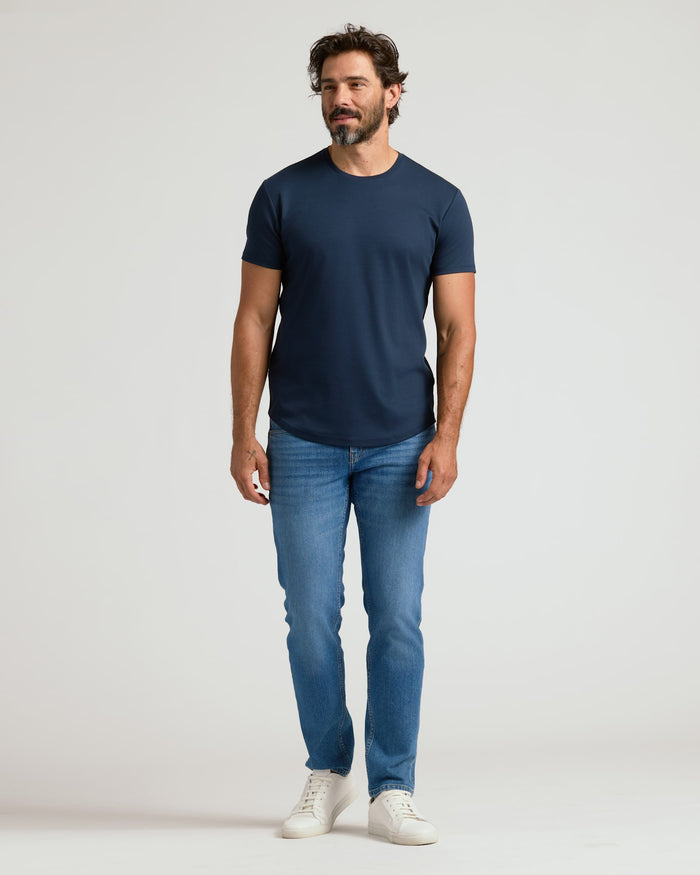 Man wearing a navy crew neck t-shirt with curved hem paired with blue jeans and white sneakers, showcasing the Pima Cotton Blend Curved Hem Crew 4-Pack men's basics.