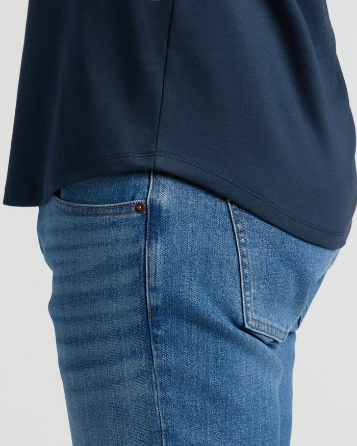 Close-up side view of a person wearing the Navy Pima Cotton Blend Curved Hem Crew paired with blue jeans, highlighting the curved hem detail on a men's basics top.
