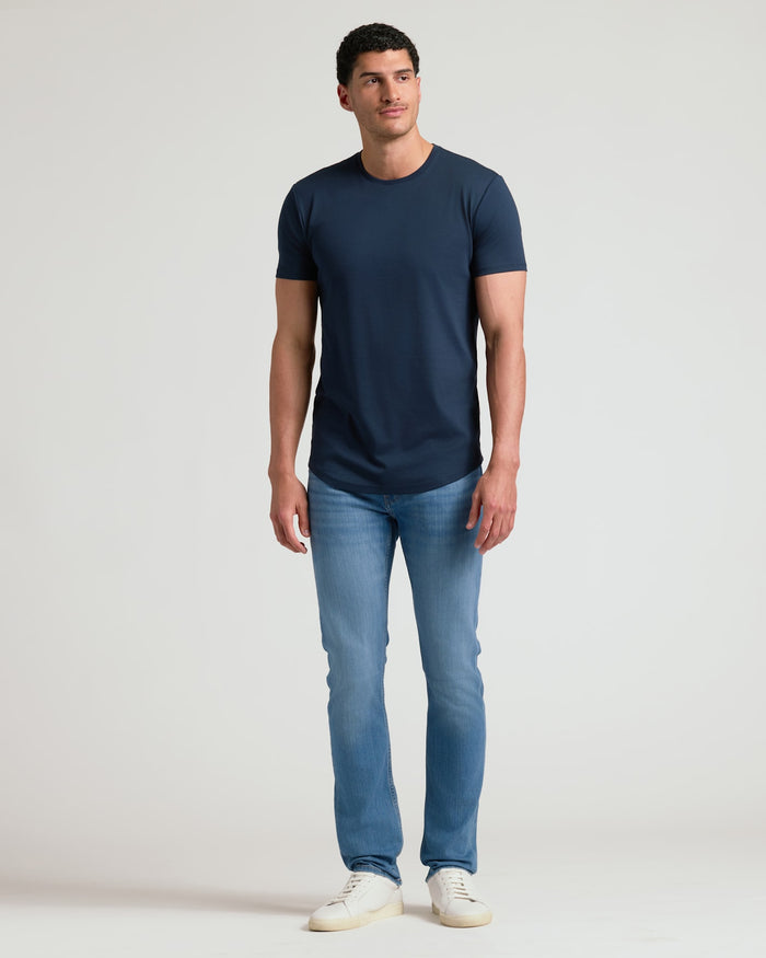 Man wearing a navy crew neck t-shirt with curved hem paired with light blue jeans and white sneakers, showcasing the Tall Pima Cotton Blend Curved Hem Crew 4-Pack in a casual style.