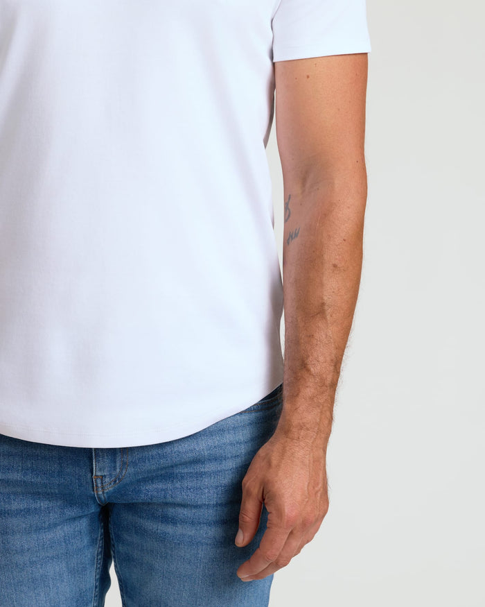 Close-up of a male model wearing a white Pima Cotton Blend Curved Hem Crew 7-Pack shirt paired with blue jeans, showcasing the curved hem detail and comfortable men's basics fit.