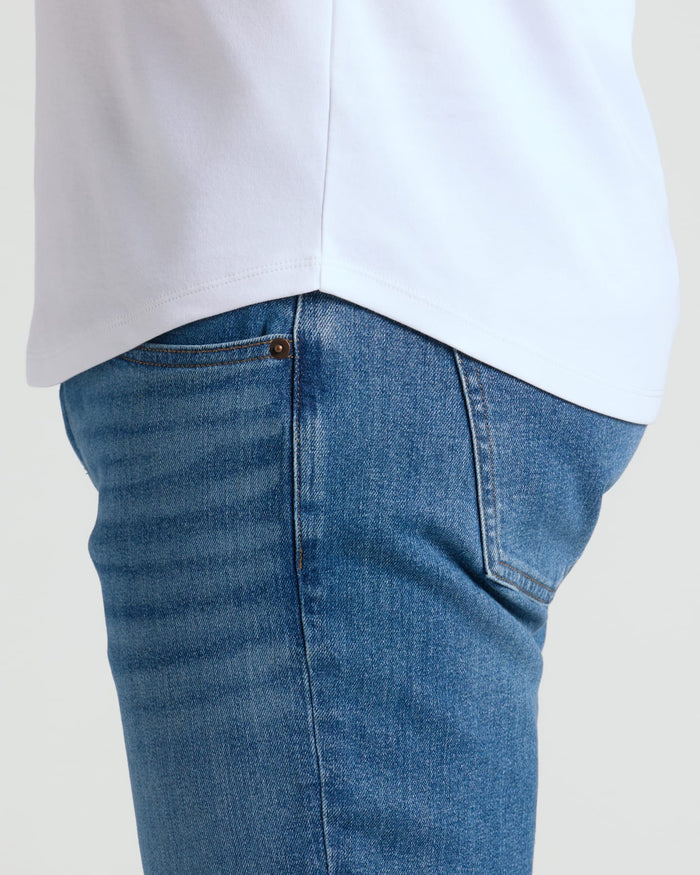 Detail close-up of a white Pima Cotton Blend Curved Hem Crew 7-Pack shirt worn untucked over blue jeans, highlighting the curved hem design and fabric texture.