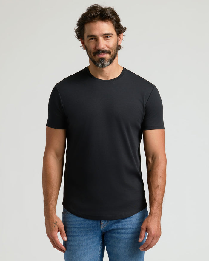 A man wearing a black Pima Cotton Blend Curved Hem Crew 4-Pack t-shirt paired with blue jeans, standing against a plain light background.