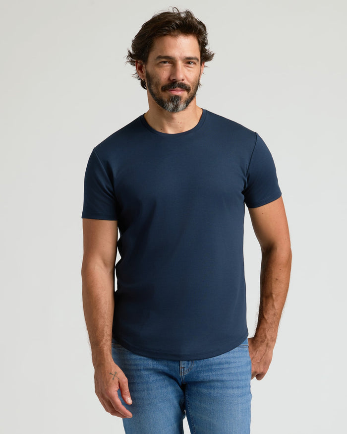 A man wearing a navy blue Pima Cotton Blend Curved Hem Crew 4-Pack t-shirt paired with light blue jeans, standing against a neutral background.