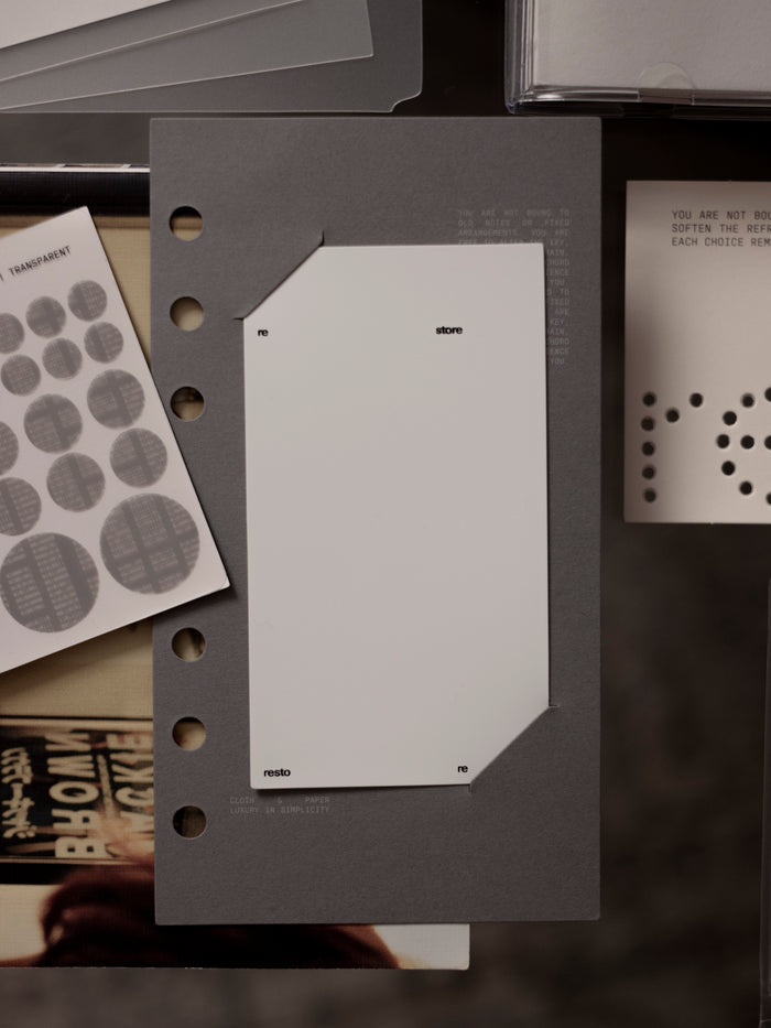 Personal sized grey matte paper dashboard with plastic layer insert into paper slits with other items around it.