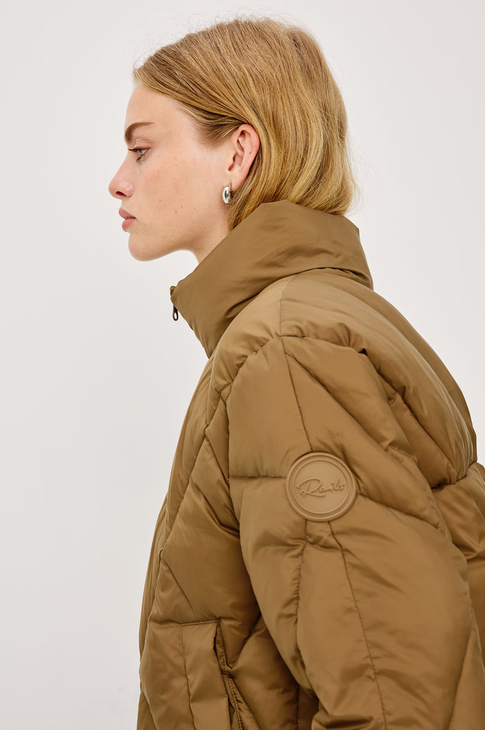 Summit Cropped Puffer Jacket With Stand Collar, Front Zipper, Quilted Detailing, Side Pockets, Tonal Branded Stamp, and Long Sleeves in Ginger Colorway - Close Up Side View Featured on Model