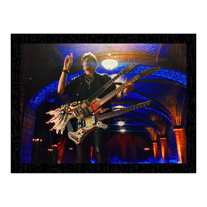 A poster featuring Steve Vai with a 3-necked guitar called, "The Hydra" in a setting with arches and a spotlight, predominantly black and blue.