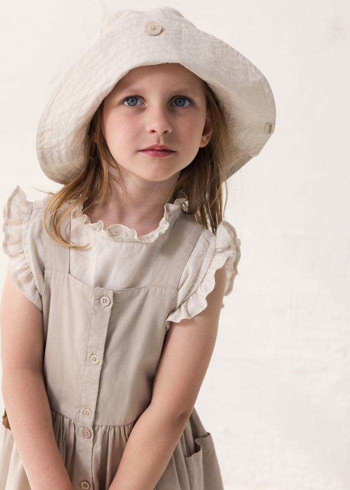 Child wearing a light dress with ruffles and a summer hat.