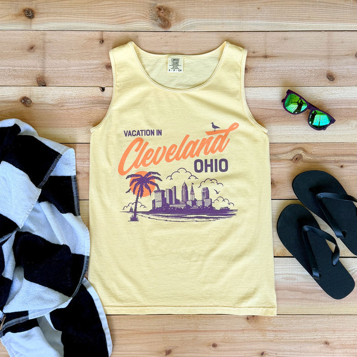 Yellow tank top with 'Vacation in Cleveland, Ohio' design on a wooden surface with sunglasses and flip-flops.
